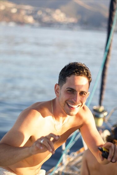 A person sitting on a boat, holding a camera, with water and a distant shoreline in the background. 4