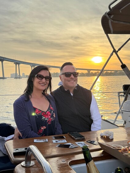 Two people on a boat with a sunset and a bridge in the background. 2