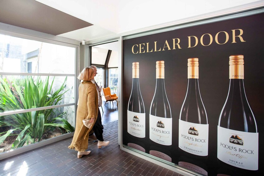 A woman walking past a Cellar Door advertisement featuring Poole's Rock wine bottles. 5