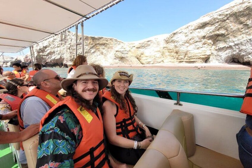 People on a boat wearing life jackets, rocky cliffs, and a beach in the background. 2