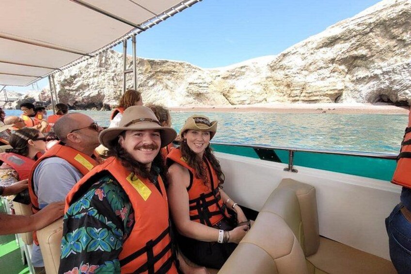 People on a boat wearing life jackets, rocky cliffs, and a beach in the background. 3