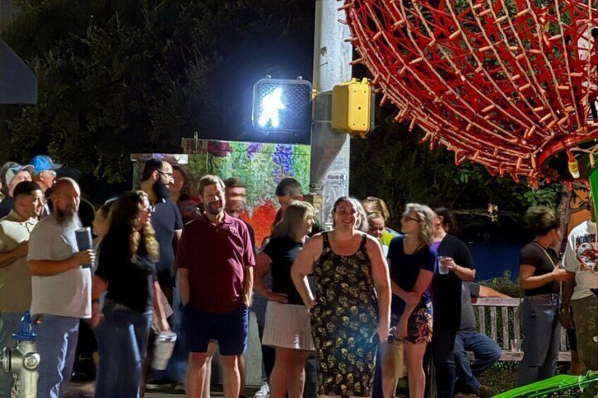 A group of people gathered outdoors at night, with a red structure and a sign with a white arrow. 3