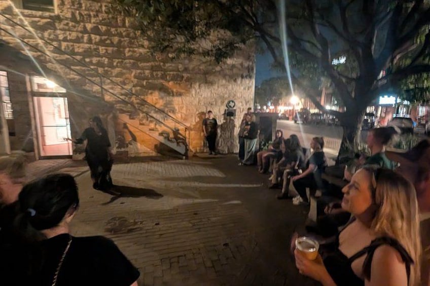 A stone building with a staircase, people sitting on benches, and a person walking. 2