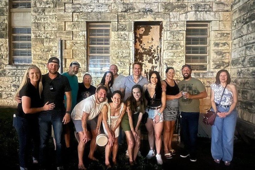 A group of people posing in front of a stone building with a weathered door and windows. 3