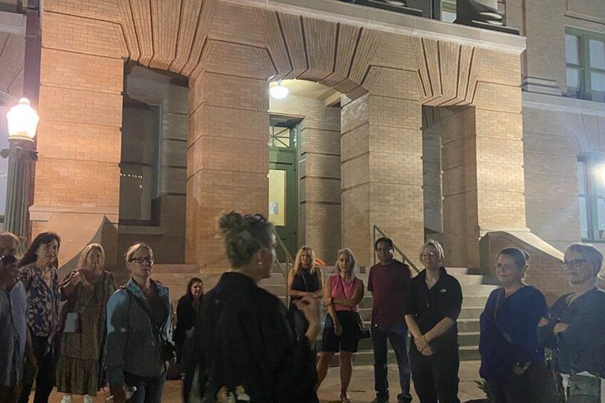 A group of people standing in front of a building with a brick facade and large columns. 1