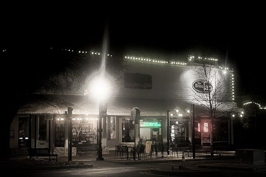 A nighttime street scene with a brightly lit building, outdoor seating, and a sign for 'The Brass Band.' 1