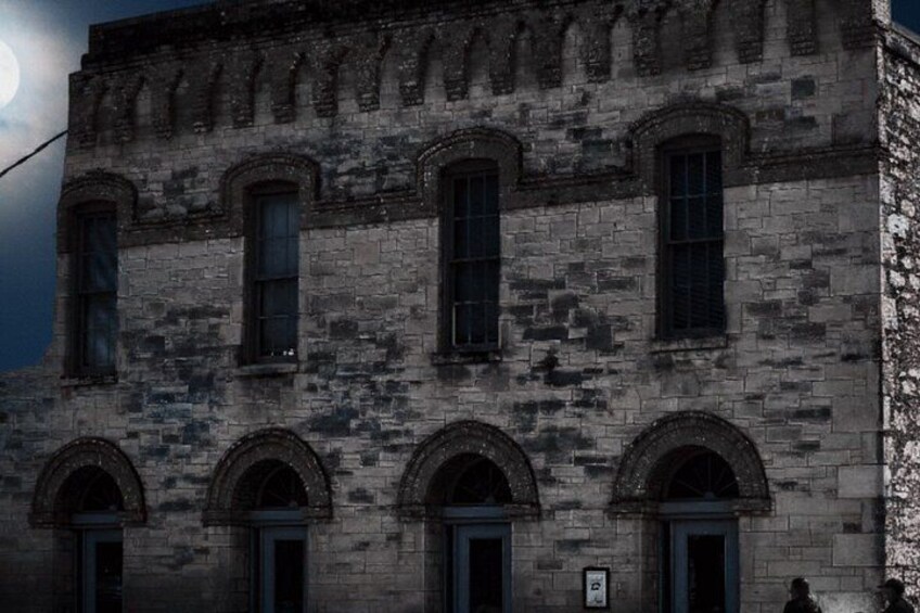 A historic stone building with arched windows and doors, under a full moon. 4
