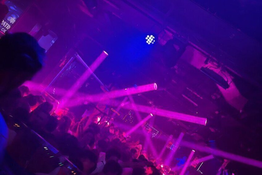A crowded indoor event with purple lighting and visible stage equipment. 5