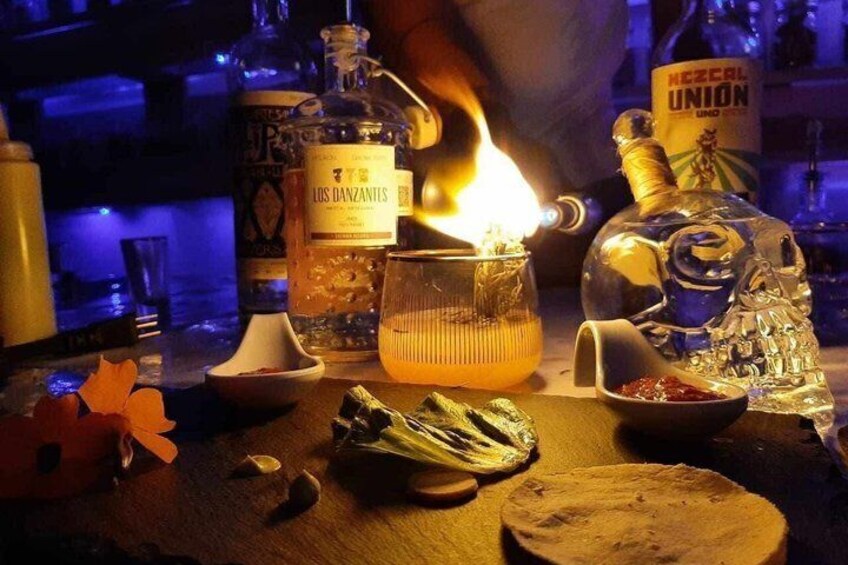 A bar setting with a lit candle, bottles of liquor, and a glass of drink on a wooden surface. 1