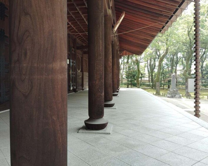 A covered walkway with large wooden columns and a tiled floor, surrounded by trees and a stone structure. 2
