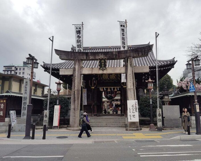 A traditional Japanese gate with banners, a pedestrian crossing, and modern buildings in the background. 3