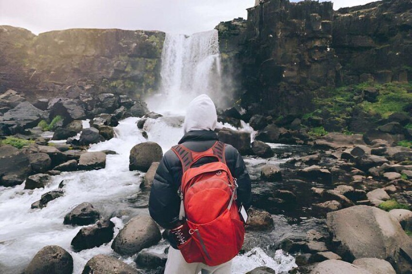 A person with a red backpack standing in front of a waterfall. 3