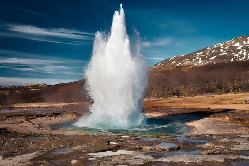 A geyser erupting in a natural landscape with a mountain in the background. 5
