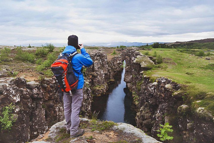 A person taking a photograph of a narrow water channel between rocky cliffs. 1