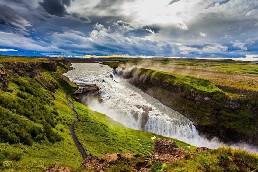 A waterfall cascading down a steep cliff surrounded by lush green grassland under a cloudy sky. 2