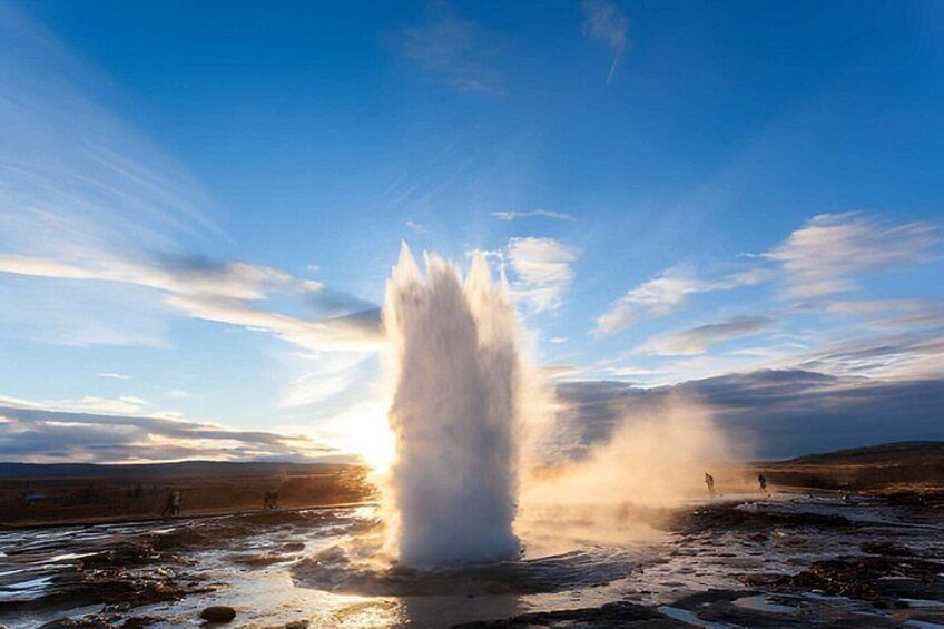 A geyser erupting with steam and water, surrounded by a flat landscape and a clear sky. 3