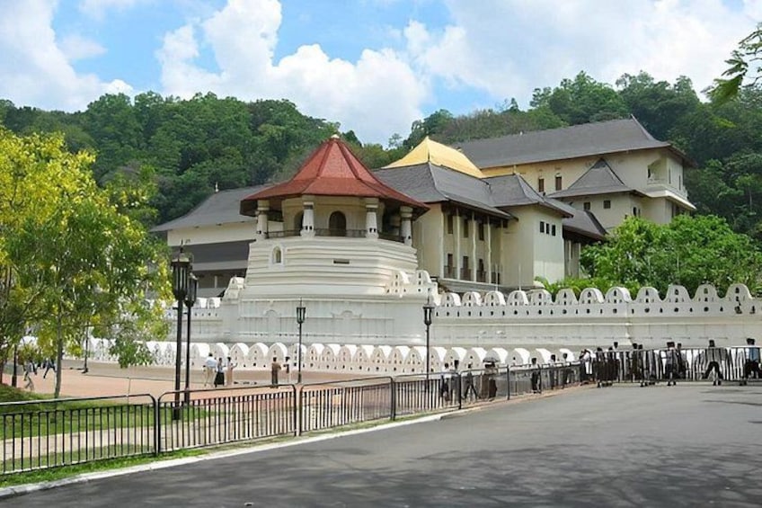 A large white building with a red roof, surrounded by a white wall with arches, set against a backdrop of green hills. 2