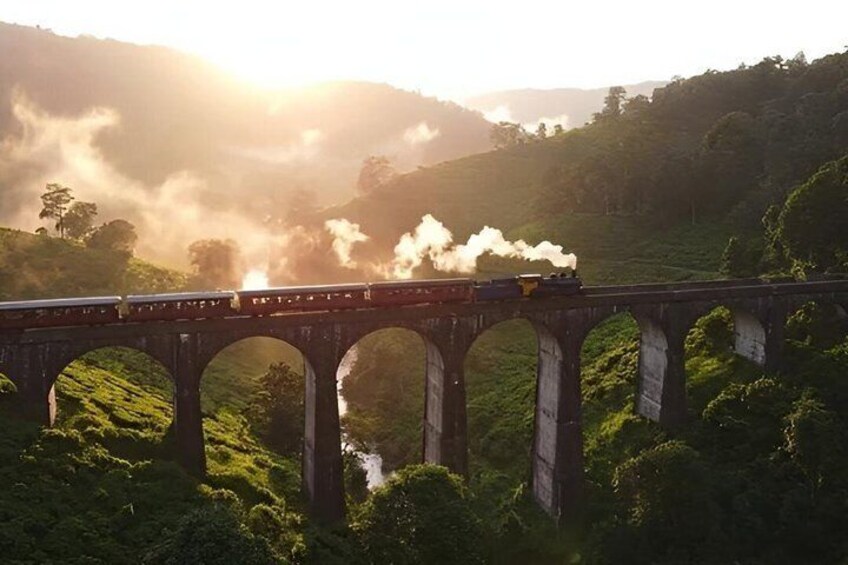 A steam train crossing a bridge over a river surrounded by lush greenery. 1