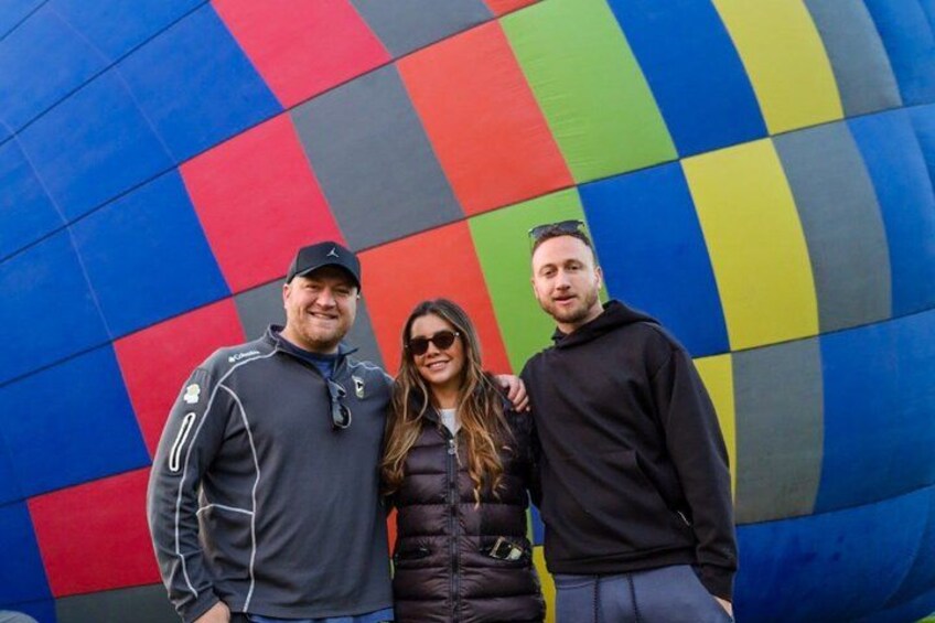 Three people standing in front of a colorful, checkered hot air balloon. 3