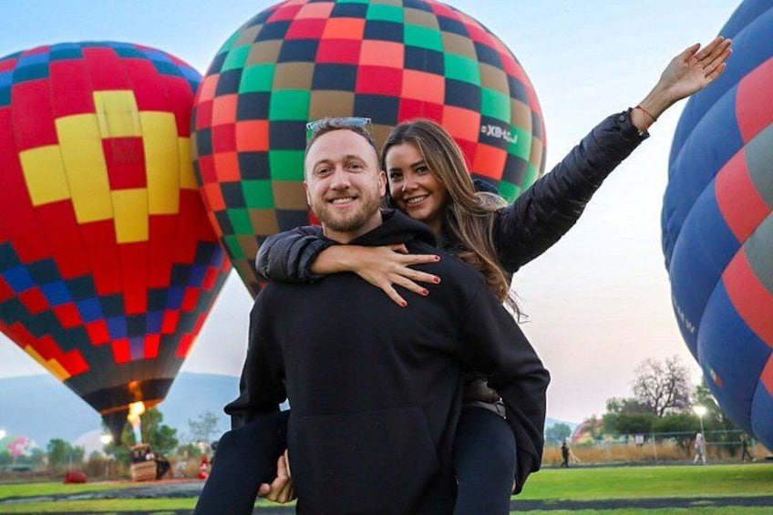 A person being carried on a hot air balloon with colorful patterns, another balloon in the background, and a grassy field. 1