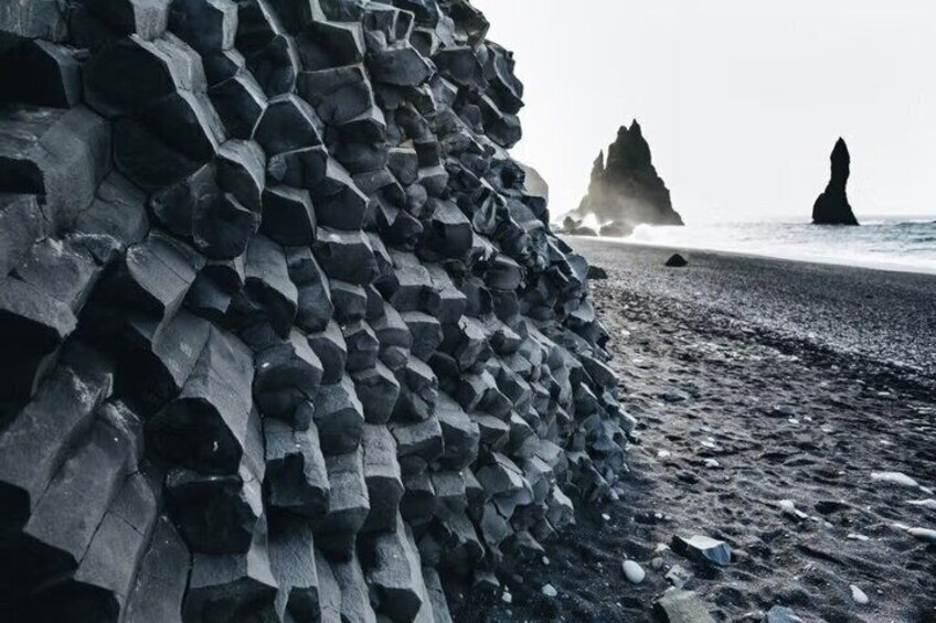 A stack of hexagonal basalt columns on a beach with distant rock formations. 3