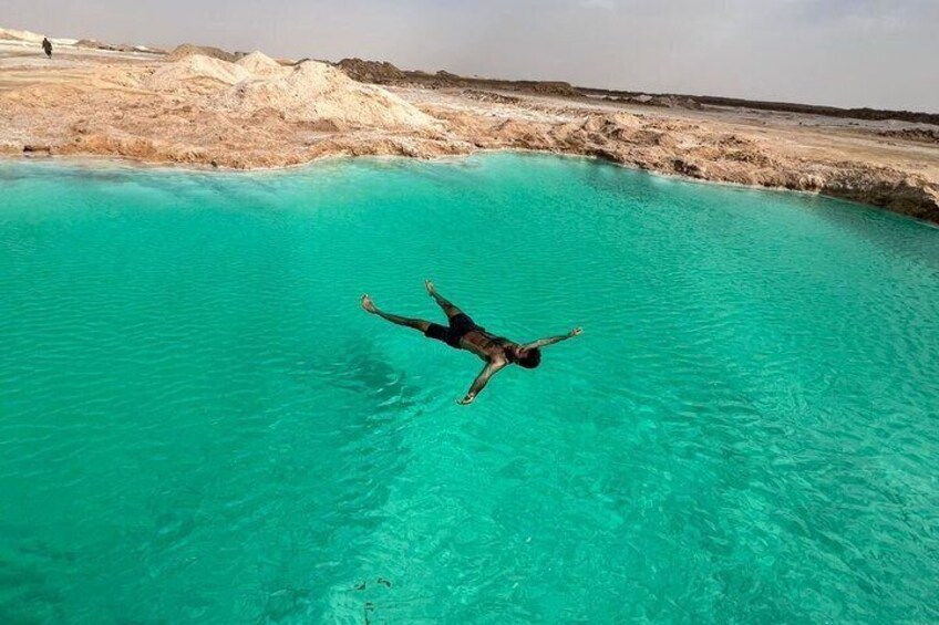 A person floating in a turquoise pool surrounded by a barren landscape. 1