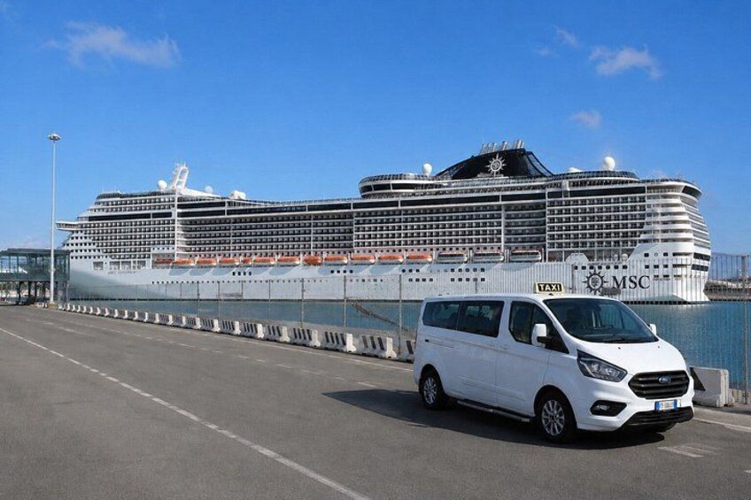 A white van parked on a road with a large cruise ship in the background. 2