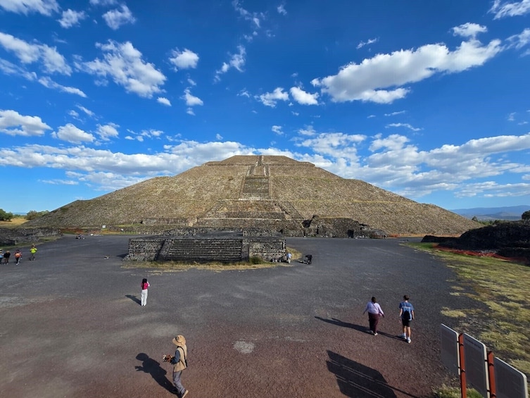 Une grande structure en forme de pyramide, avec un sommet plat, entourée d’une zone pavée où l’on voit des gens se promener, et un ciel bleu dégagé. 4