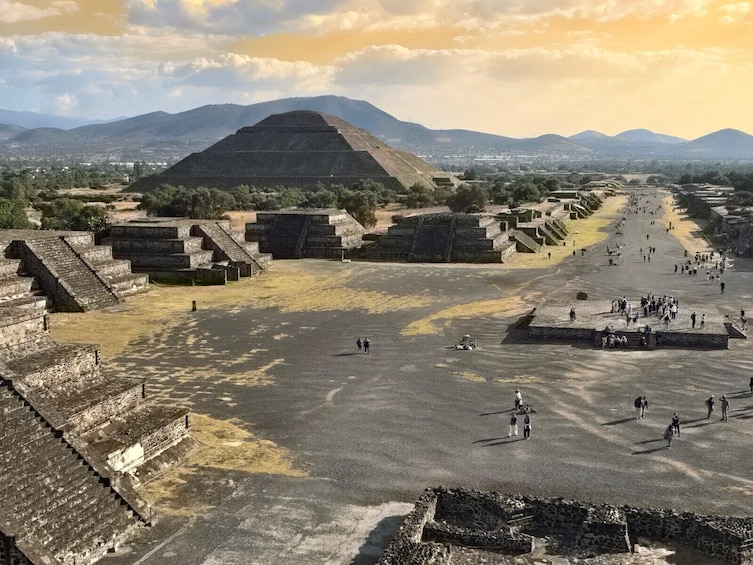 Une grande pyramide et des structures à gradins se dressent sur un site historique, avec une chaîne de montagnes visible au loin. 5