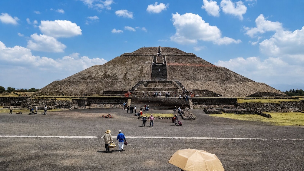 Une grande pyramide dotée d’un escalier menant à son sommet, entourée d’une zone plane où des personnes se promènent et se tiennent debout. 3
