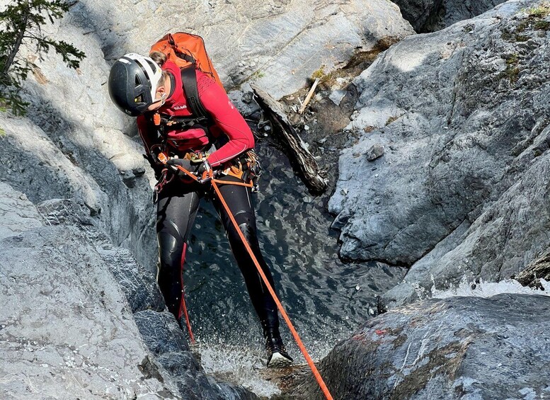 A person climbing a rocky terrain with a helmet and red gear. 1