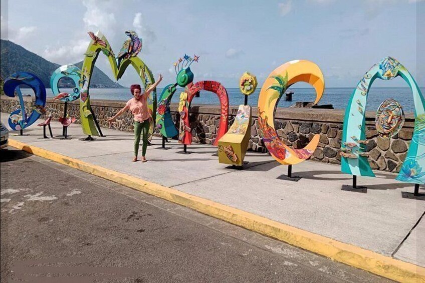A person standing in front of colorful, abstract sculptures on a seaside promenade. 3