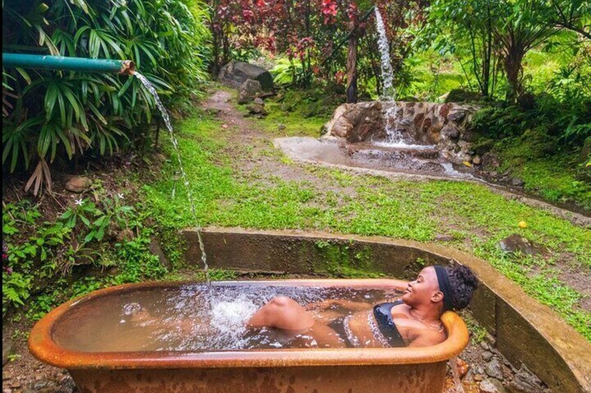 A person relaxing in a hot tub surrounded by lush greenery and a small waterfall. 2