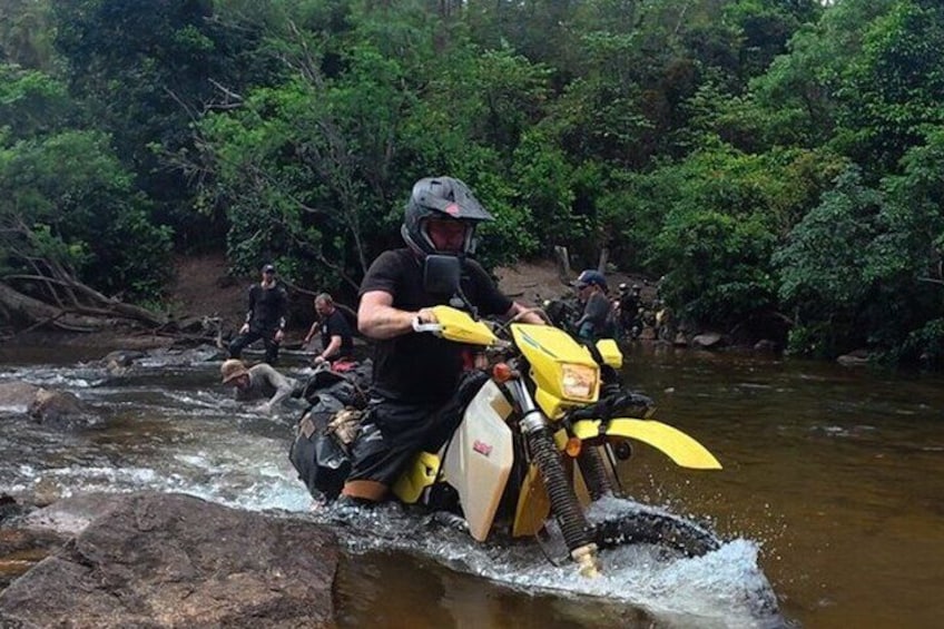 A person on a yellow motorcycle navigating a river. 1