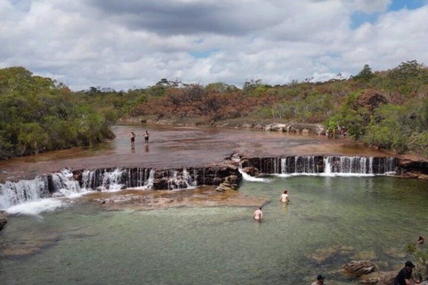 A waterfall, clear water, and people swimming. 3