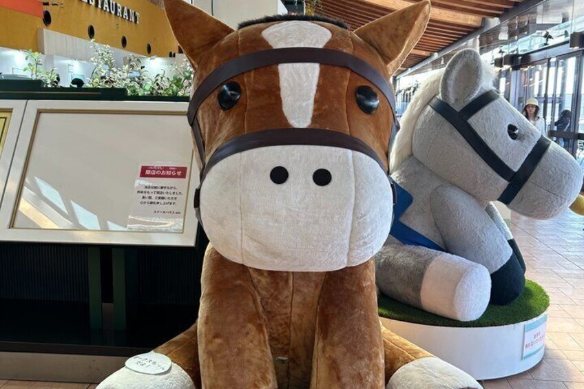 A brown horse with a white face and black eyes, sitting on a white cushion with a green base. 4