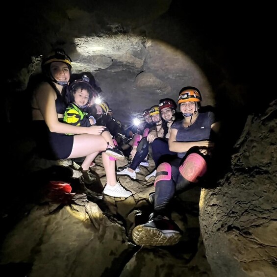 People sitting in a cave with helmets and flashlights. 3