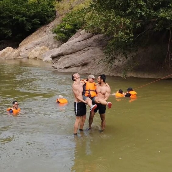 People in a river, some carrying others, with rocks and greenery in the background. 2