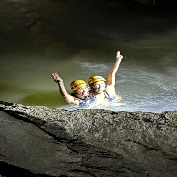 Two people in a water body wearing helmets, with one raising an arm. 5