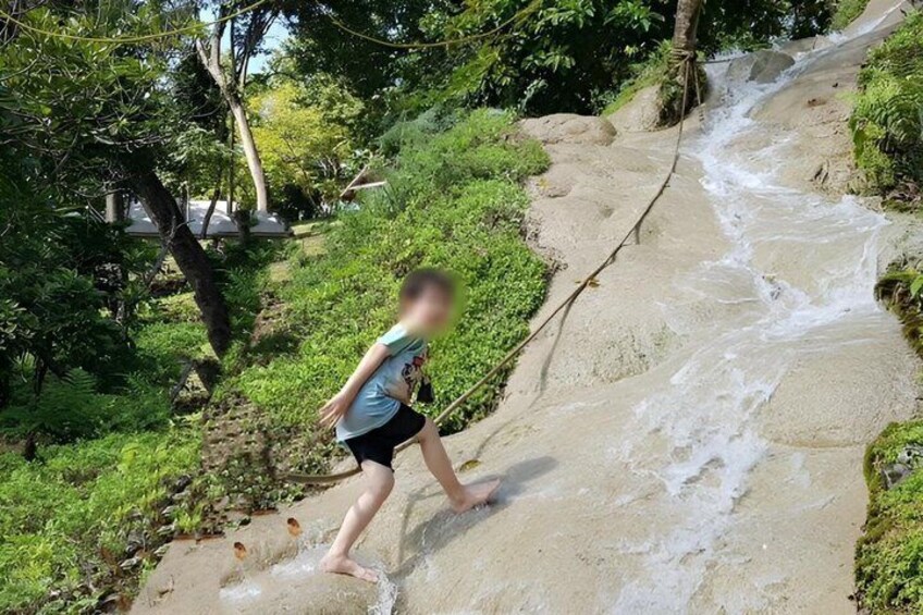 A person walking on a sandy path beside a flowing stream in a forested area. 3
