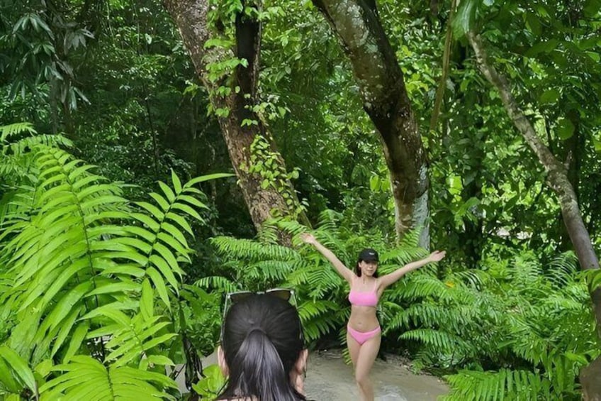 A person in a pink bikini standing in a forest with arms raised. 2