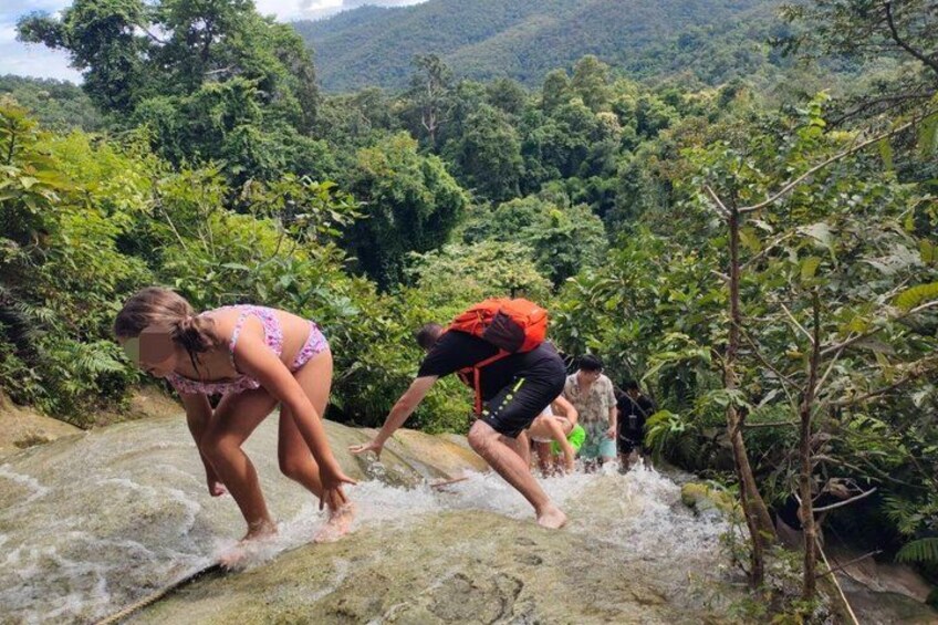 Two people jumping into a river, surrounded by lush greenery and a mountainous landscape. 1