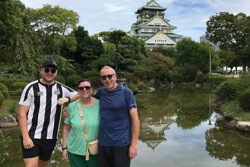 Three people standing in front of a castle with a pond behind them. 4