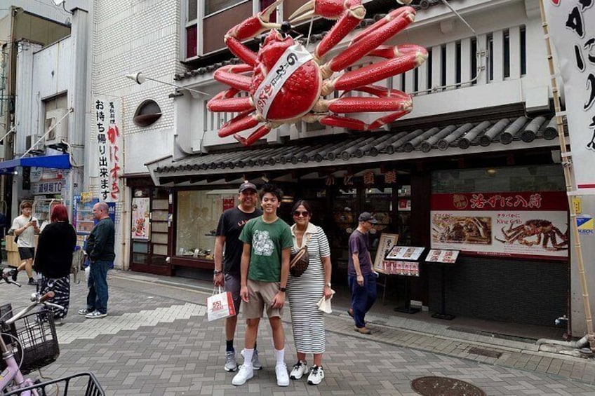 A street with a large red crab decoration, a storefront with Japanese signage, and pedestrians. 3