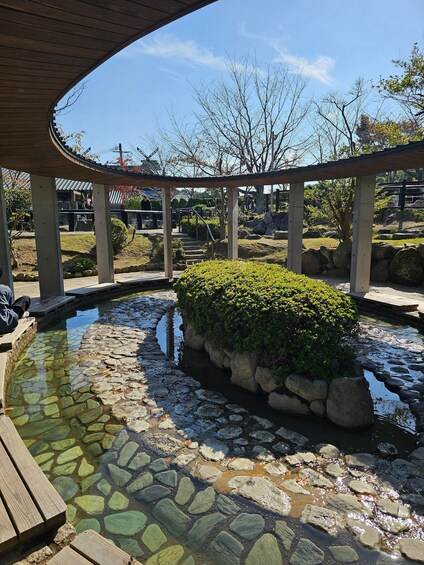A stone-lined pond with a wooden deck, surrounded by rocks and greenery under a wooden pavilion. 4