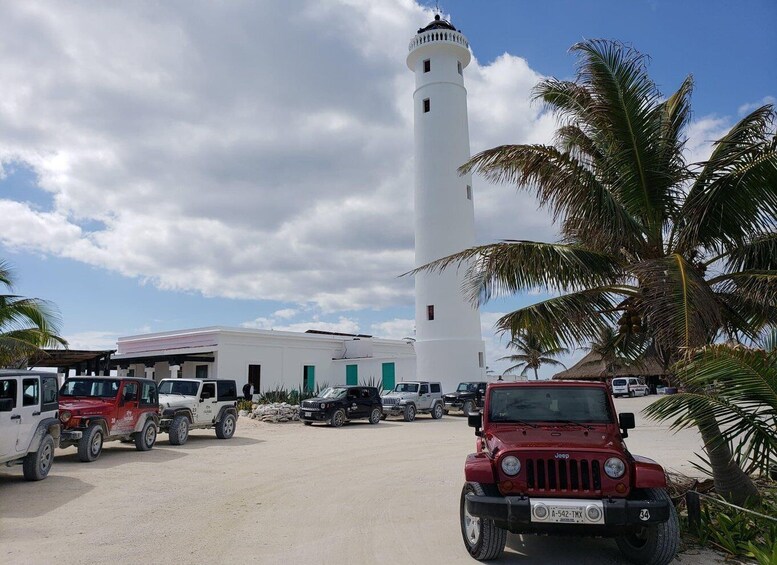 A white lighthouse, parked vehicles, and palm trees. 4