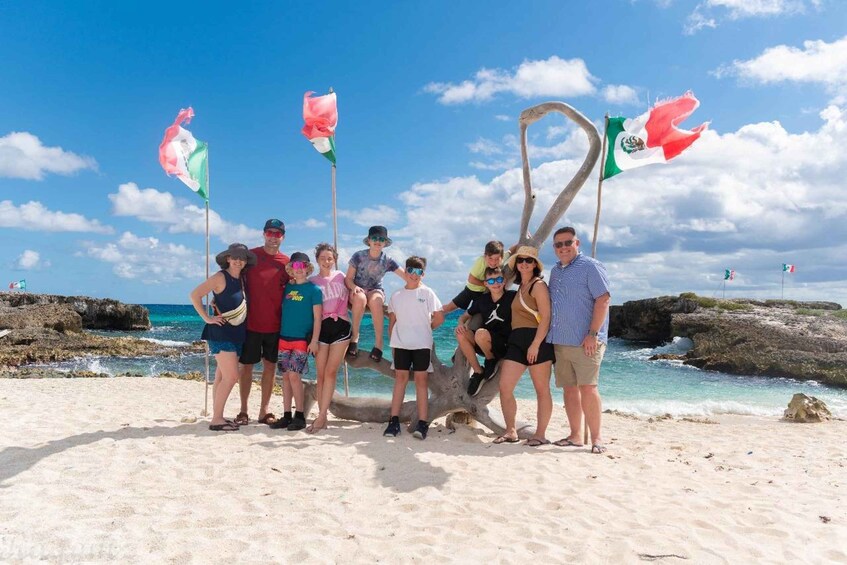 A group of people standing on a sandy beach with a rocky shoreline and clear blue sky. 2