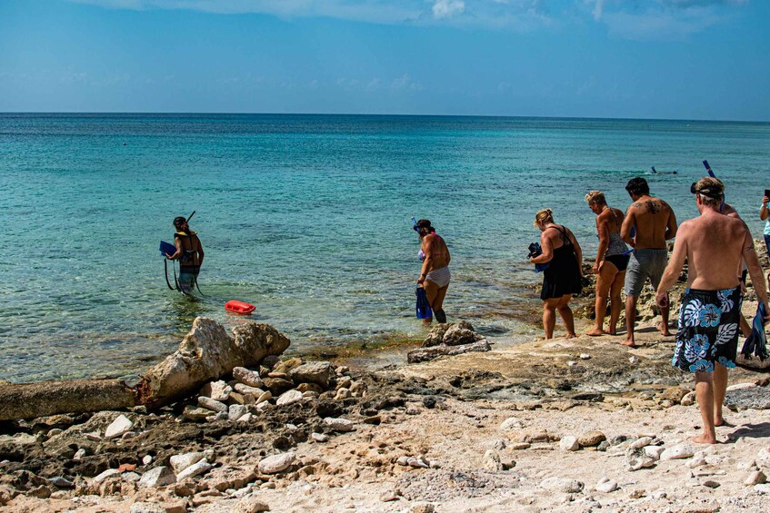 A rocky beach with clear turquoise water, people standing and swimming, and a diver in the water. 5