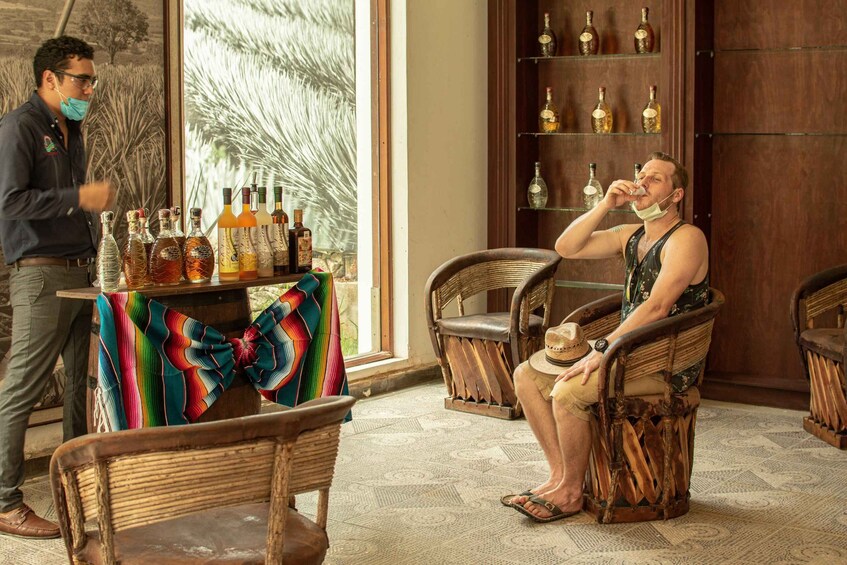 A man sitting on a chair in a room with a wooden cabinet filled with bottles. 1