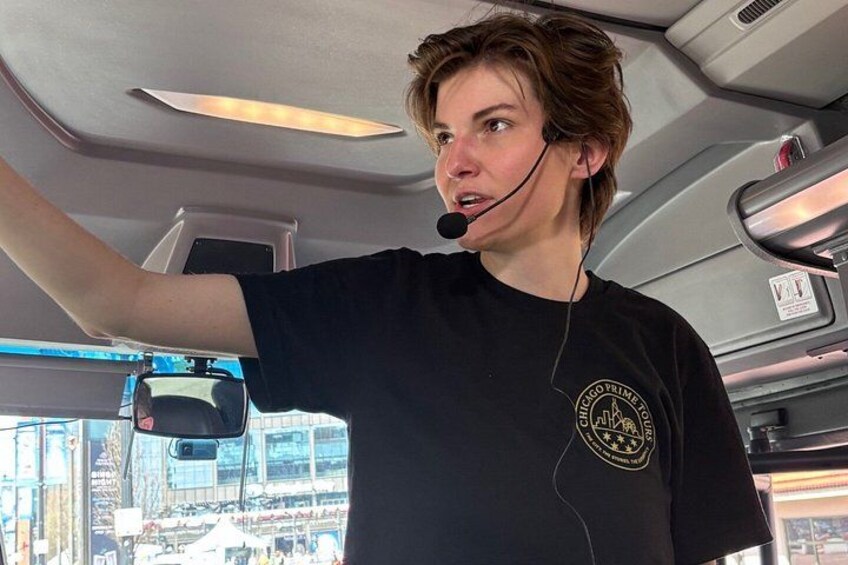 A person in a black shirt with a logo, inside a vehicle with a view of a cityscape through the window. 5